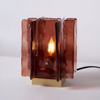 Straight-on view of a lit Clérachic table lamp, with a candle-style bulb glowing inside its amber-red glass panels and a black cord at the side.