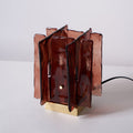 An unlit Clérachic table lamp with amber-red glass panels and a brass base stands on a white tabletop with its black cord trailing to the right.