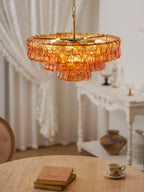 Amber glass tiles glow on this Clérachic chandelier, hung over a round stone-topped table set with a book and a teacup.