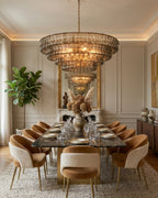 Over a long glass-topped dining table with suede and boucle chairs hangs this smoke-grey Clérachic chandelier, a mirror behind it.