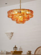 Against a pale plastered wall, the amber glass tiers of this Clérachic chandelier glow, with a book and cup on a table below.