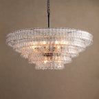 Five stepped tiers of clear glass on this Clérachic chandelier, with a black stem and warm bulbs glowing, on a taupe backdrop.