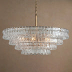 Clear textured glass tiers on a Clérachic chandelier with a brass stem, hung unlit against a warm taupe backdrop.