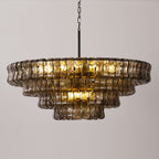 The smoke-grey glass tiers of this Clérachic chandelier hang on a black chain, glowing warm at the centre against pale grey.