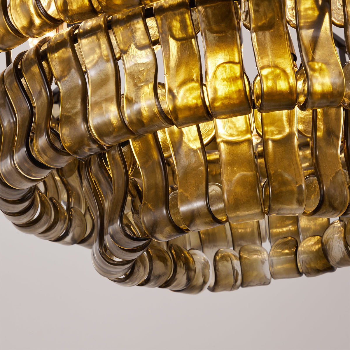 Close view of the wavy smoke-grey glass tiles on this Clérachic chandelier, lit warm gold from within.