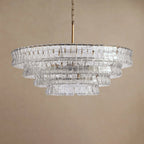 Clear glass chandelier from Clérachic, hung on a brass chain and stem in front of a sand-coloured backdrop.
