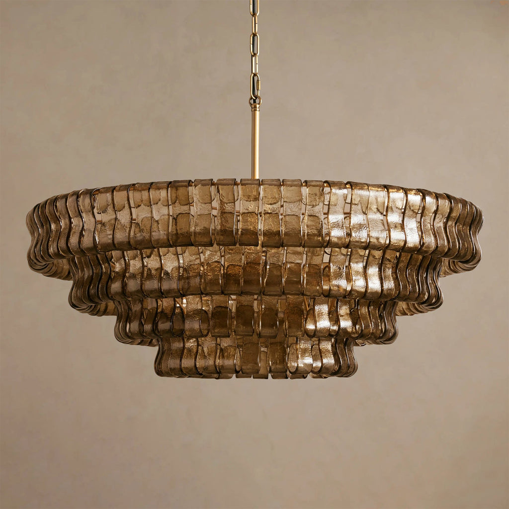Five stepped tiers of smoke-grey glass make up this Clérachic chandelier, with a brass chain above, on a soft beige backdrop.