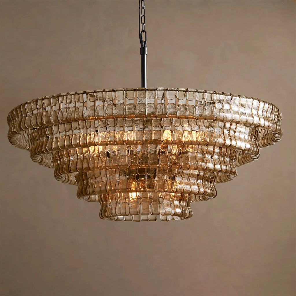 Pale champagne-toned glass tiers on a Clérachic chandelier with a black stem, lit softly against a warm tan backdrop.