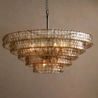 Pale champagne-toned glass tiers on a Clérachic chandelier with a black stem, lit softly against a warm tan backdrop.