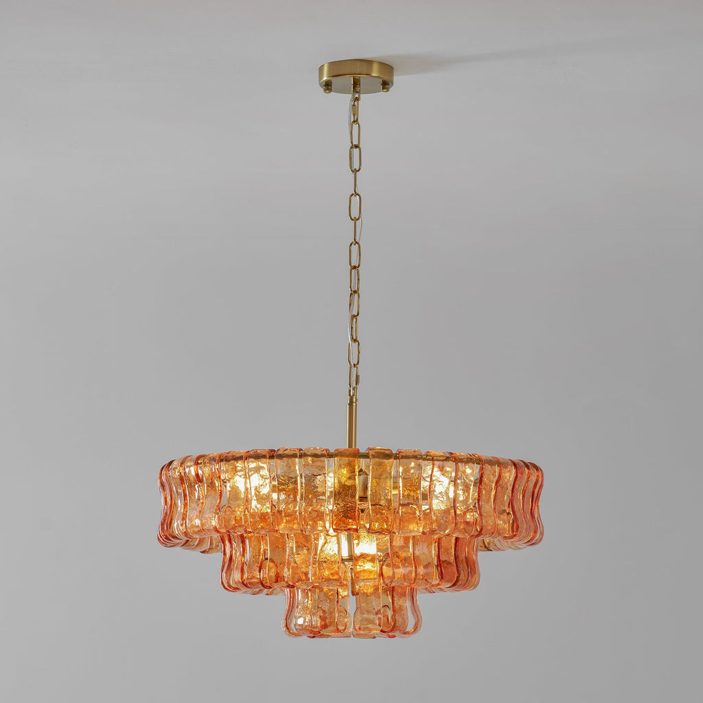 Amber-peach glass tiers on a Clérachic chandelier hung from a brass canopy and chain, against a light grey wall.