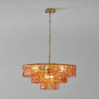 Amber-peach glass tiers on a Clérachic chandelier hung from a brass canopy and chain, against a light grey wall.