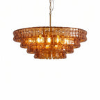 Orange-amber glass on this Clérachic chandelier is lit brightly inside, hung from a brass stem on a white backdrop.