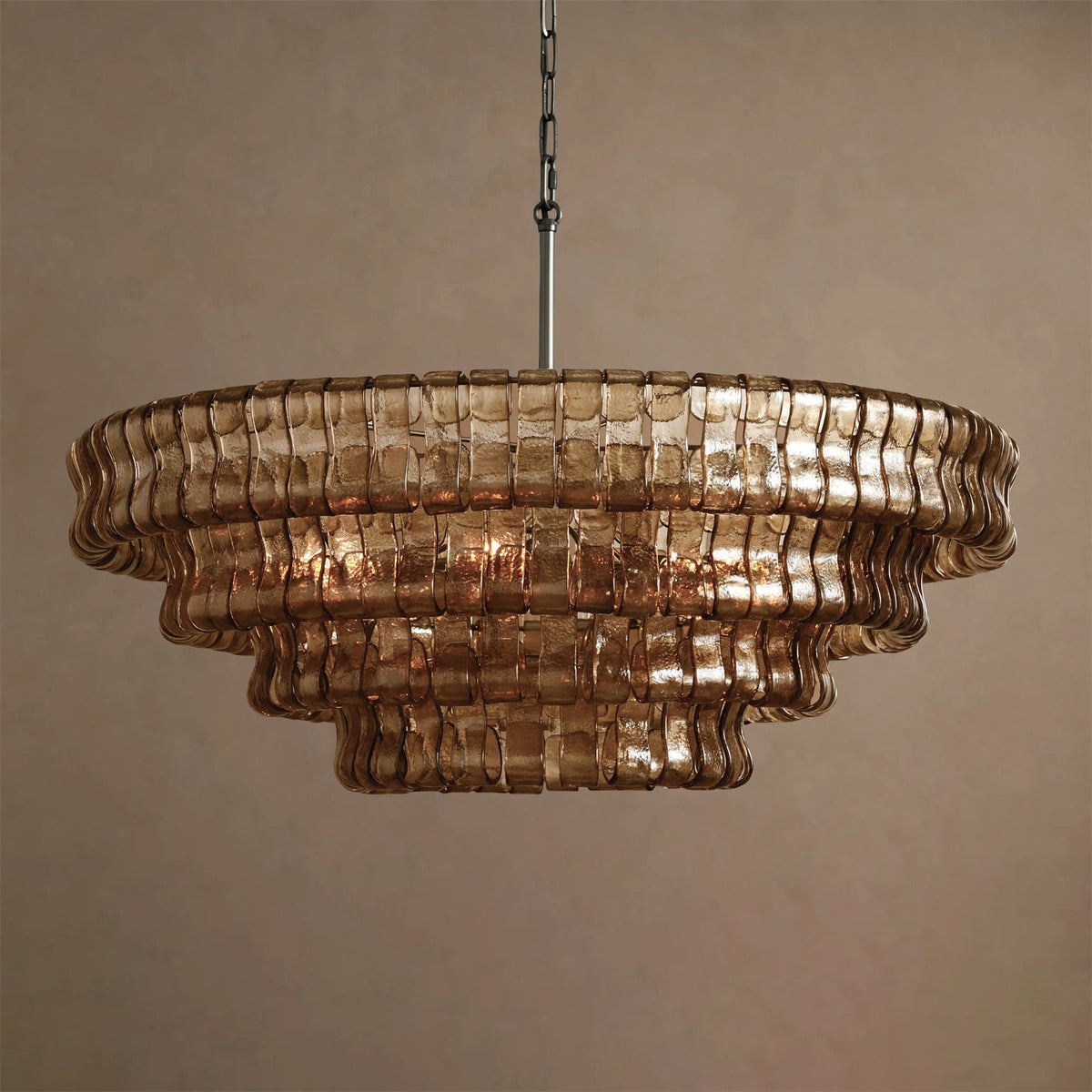 Brown-bronze Clérachic chandelier with five stepped glass tiers and a hint of warm light, on a tan backdrop.
