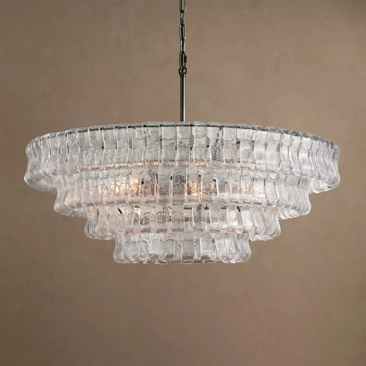 Clear glass tiers on this Clérachic chandelier, with a black chain, softly lit against a taupe backdrop.