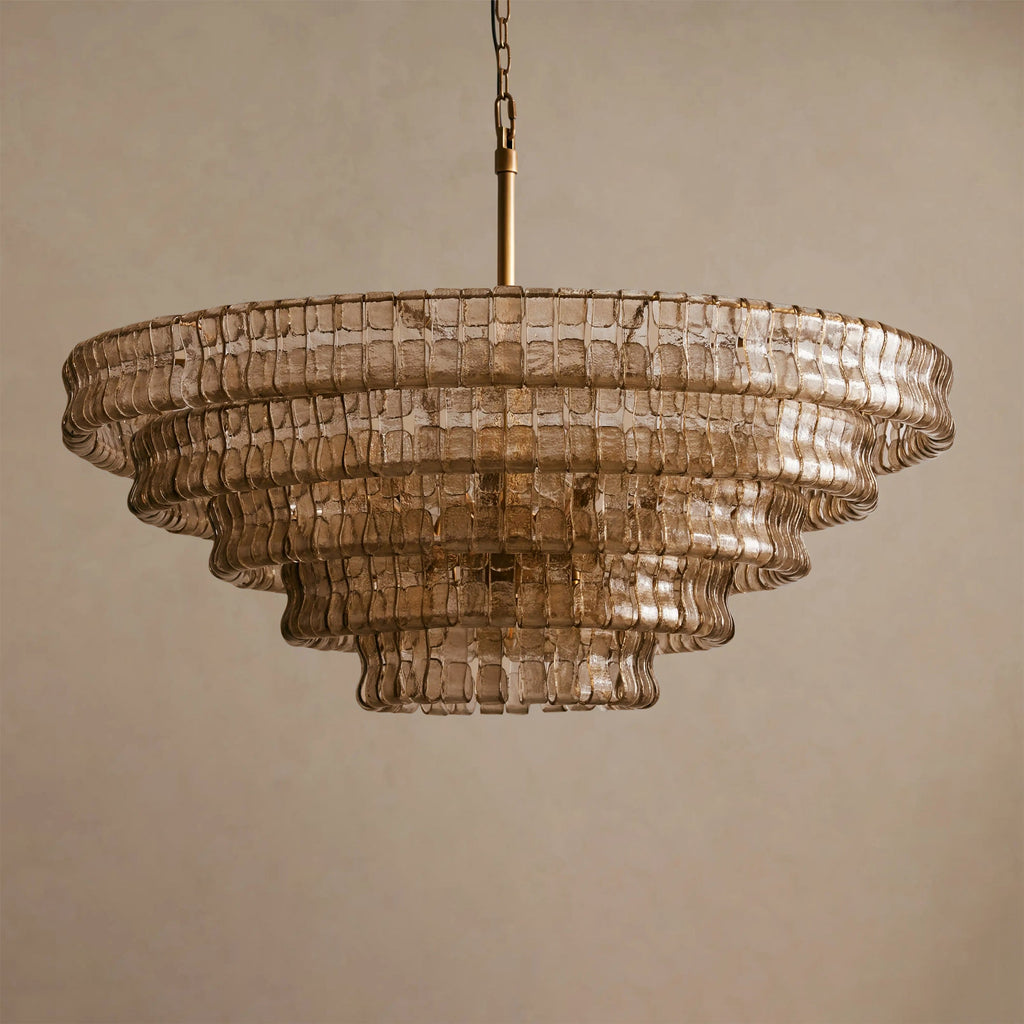 Smoky tan glass chandelier from Clérachic, with five tiers and a brass stem, against a beige backdrop.