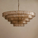 Smoky tan glass chandelier from Clérachic, with five tiers and a brass stem, against a beige backdrop.