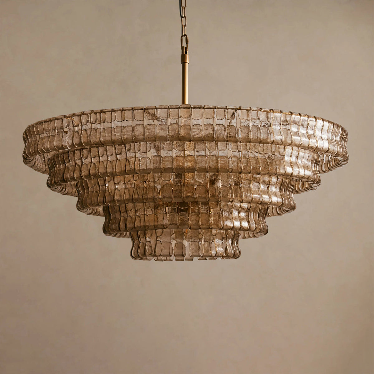 Smoky tan glass chandelier from Clérachic, with five tiers and a brass stem, against a beige backdrop.