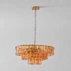 Peach-amber glass Clérachic chandelier hanging from a brass ceiling plate and chain, against a light grey wall.