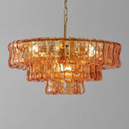 Lit close up, an amber-peach glass Clérachic chandelier on a brass stem is set against a grey backdrop.