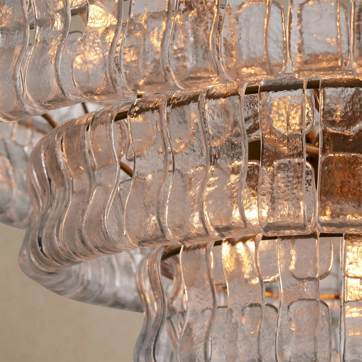 Close view of the clear, rippled glass strips layered in tiers on this Clérachic chandelier, with warm light behind.