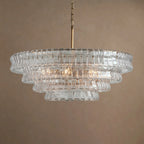 Four tiers of clear glass on this Clérachic chandelier with a brass stem, hung against a warm beige backdrop.