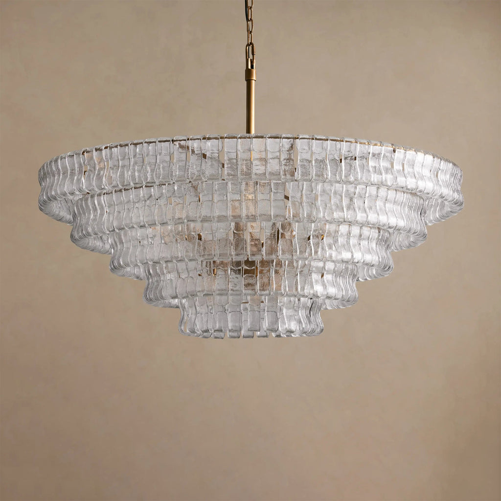 On a brass stem, the five tiers of this clear glass Clérachic chandelier narrow toward the base, against a sand backdrop.