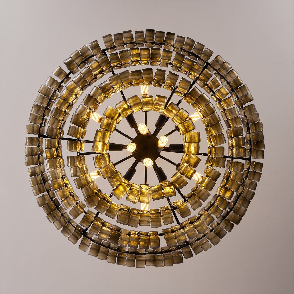 Looking straight up at a Clérachic chandelier, concentric rings of smoke-grey glass tiles circle a black spoked hub with bulbs.