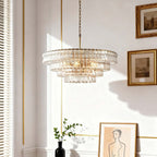 In a bright room with white walls, gold trim and framed pictures, a clear glass chandelier from Clérachic hangs above a black vase.