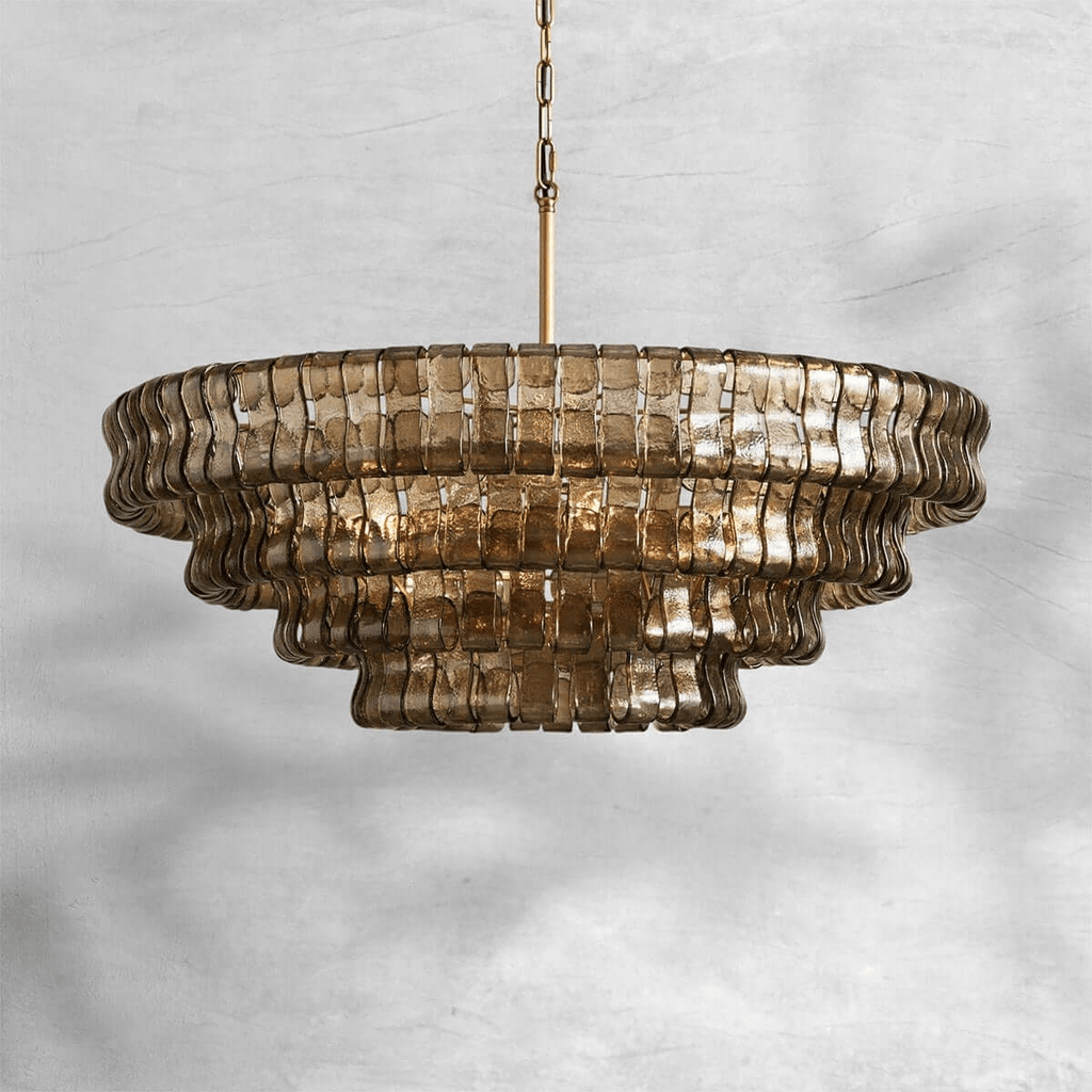 Smoke-grey glass chandelier from Clérachic on a brass stem, hung against a pale marbled grey backdrop.