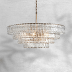 A clear glass Clérachic chandelier with a brass stem, shown against a pale marbled grey backdrop.