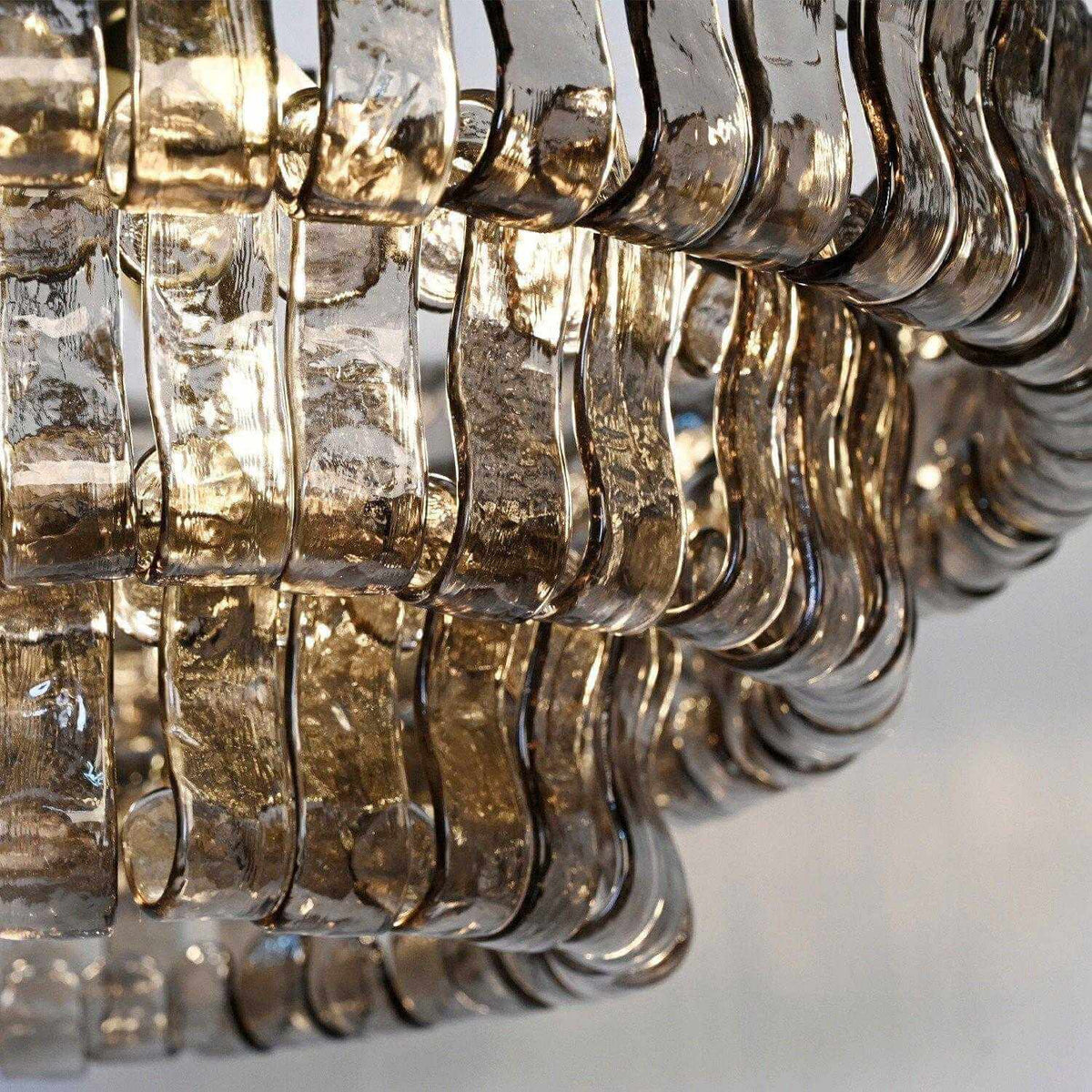 Close view of rippled smoke-grey glass strips curling at the edge of this Clérachic chandelier, against pale grey.