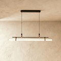 Clérachic linear pendant in black with a glowing white tube on leather straps, hung from a slim oval canopy on two cords.