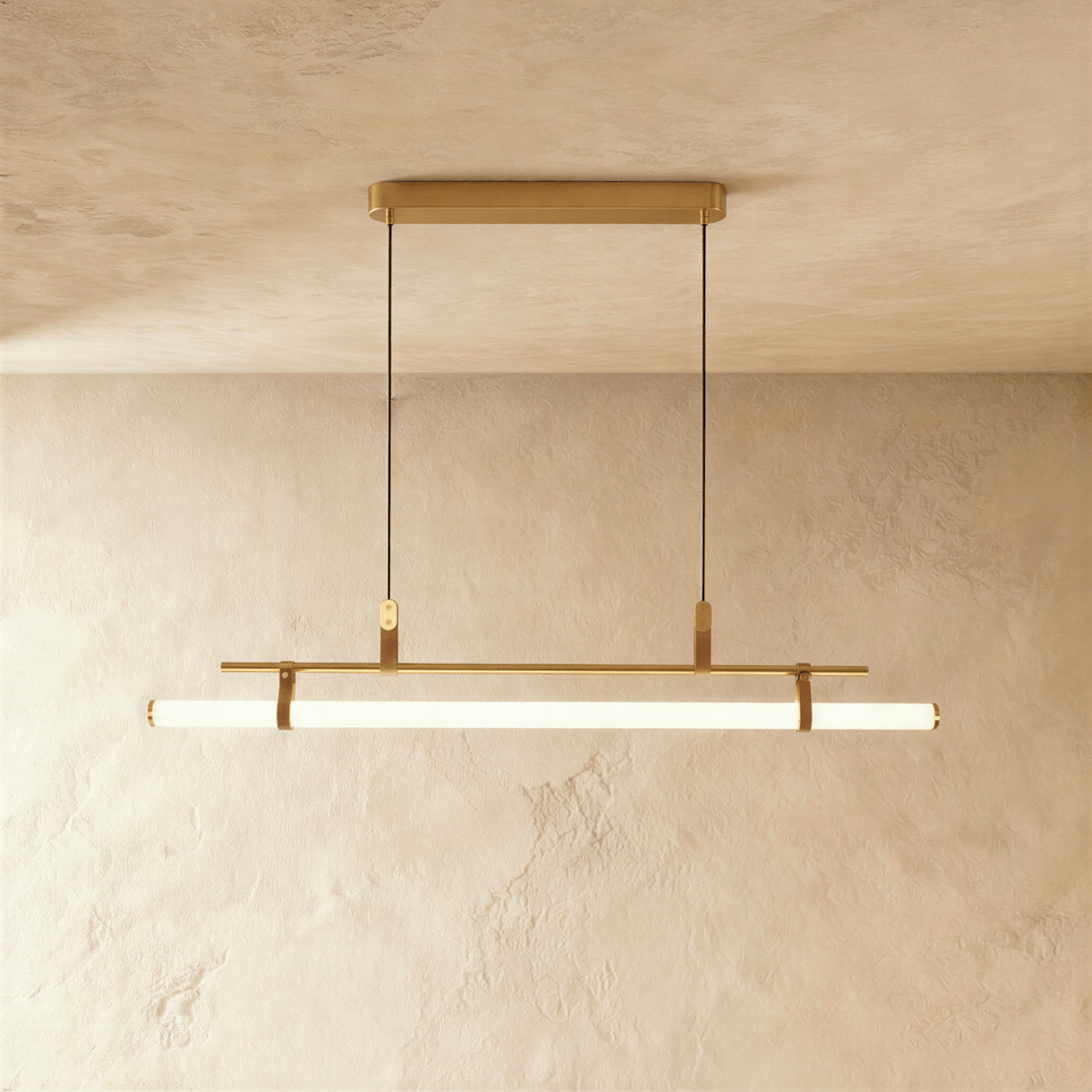 Clérachic linear pendant in brushed gold with a lit opal tube on tan straps, hung from a slim gold oval ceiling canopy.