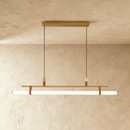 Clérachic longer gold linear pendant with a glowing white tube on leather straps, hung from a gold canopy on two cords.