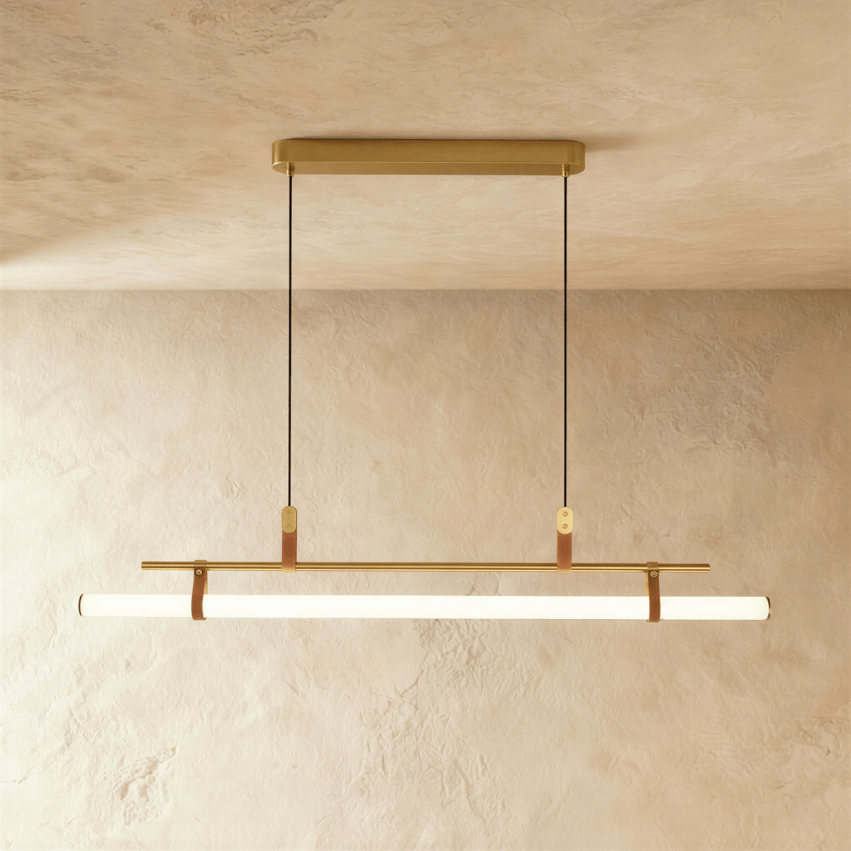 Clérachic longer gold linear pendant with a glowing white tube on leather straps, hung from a gold canopy on two cords.