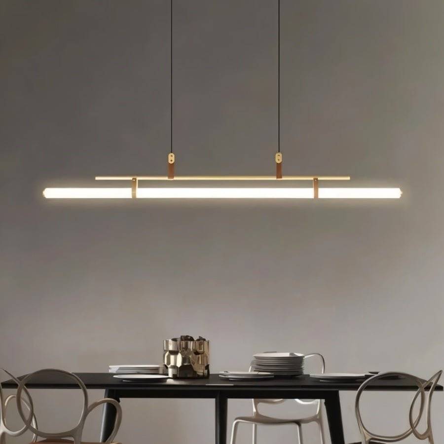 Clérachic gold linear pendant glowing above a black dining table with sculptural chairs, against a grey wall.