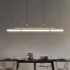 Clérachic gold linear pendant glowing above a black dining table with sculptural chairs, against a grey wall.