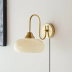 Clérachic glass wall lamp in copper and beige, plug-in cord hanging beside a dark picture frame.
