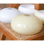 Clérachic glass wall lamp shades in beige and white, four glossy domes stacked on a rattan chair seat.