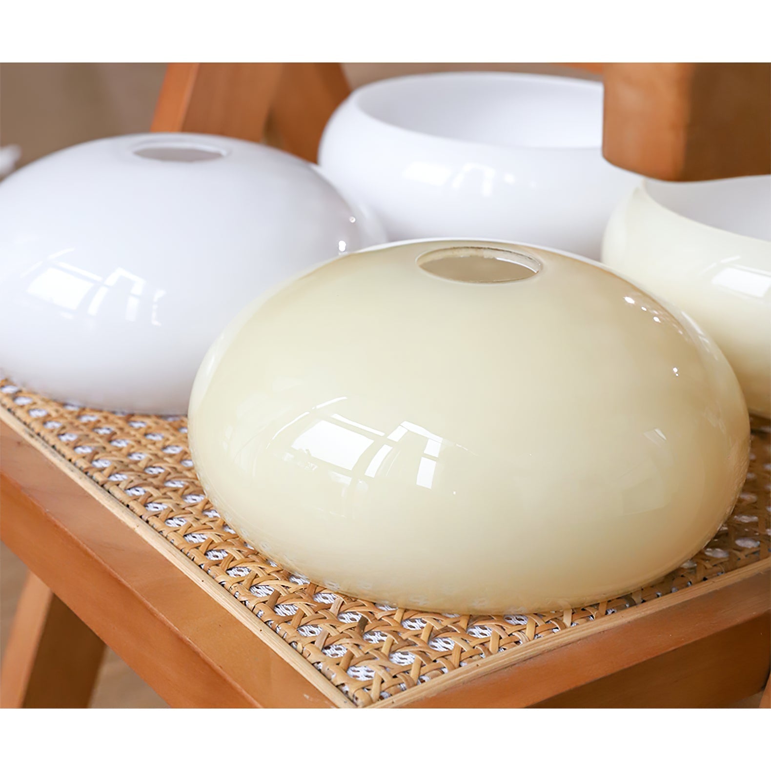 Clérachic glass wall lamp shades in beige and white, four glossy domes stacked on a rattan chair seat.