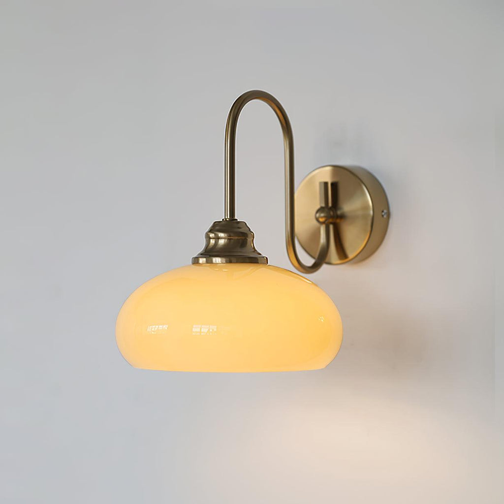 Clérachic glass wall lamp, copper arm and lit beige glass, hardwired on a plain pale wall.