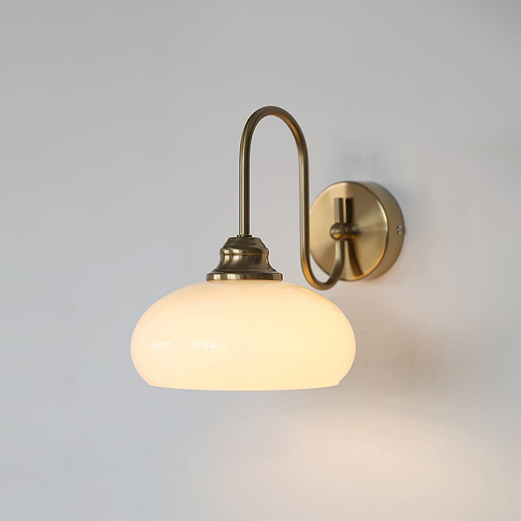 Clérachic glass wall lamp in copper with a lit white glass dome, hardwired on a pale wall.