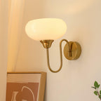 Clérachic glass wall lamp, copper arm and lit white glass, hardwired above terracotta art and a plant.