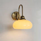 Clérachic glass wall lamp, copper J-arm and lit beige glass, hardwired with a bright pool under the shade.
