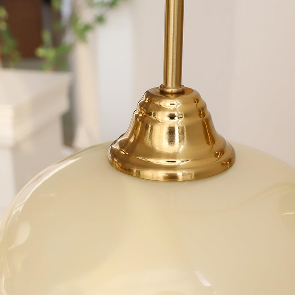 Clérachic glass wall lamp close-up: copper cap seated on glossy beige glass, foliage soft in the background.