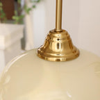 Clérachic glass wall lamp close-up: copper cap seated on glossy beige glass, foliage soft in the background.