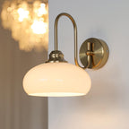 Clérachic glass wall lamp, copper crook arm and lit beige glass, hardwired with a warm light blurred behind.