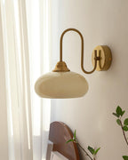Clérachic glass wall lamp in copper and beige, hardwired in daylight above a rounded wood headboard.