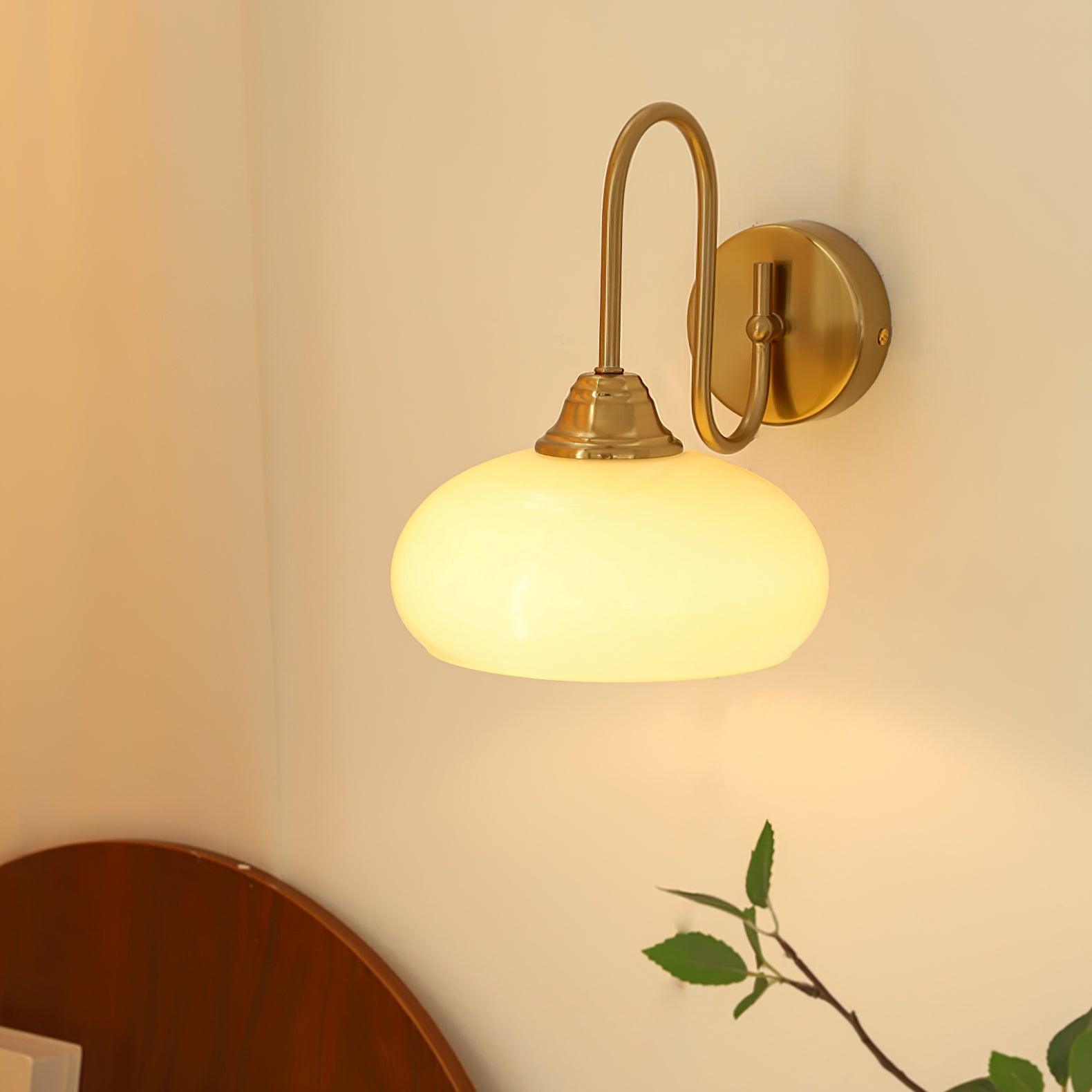 Clérachic glass wall lamp, copper and lit beige glass, hardwired above a dark headboard with a plant sprig.