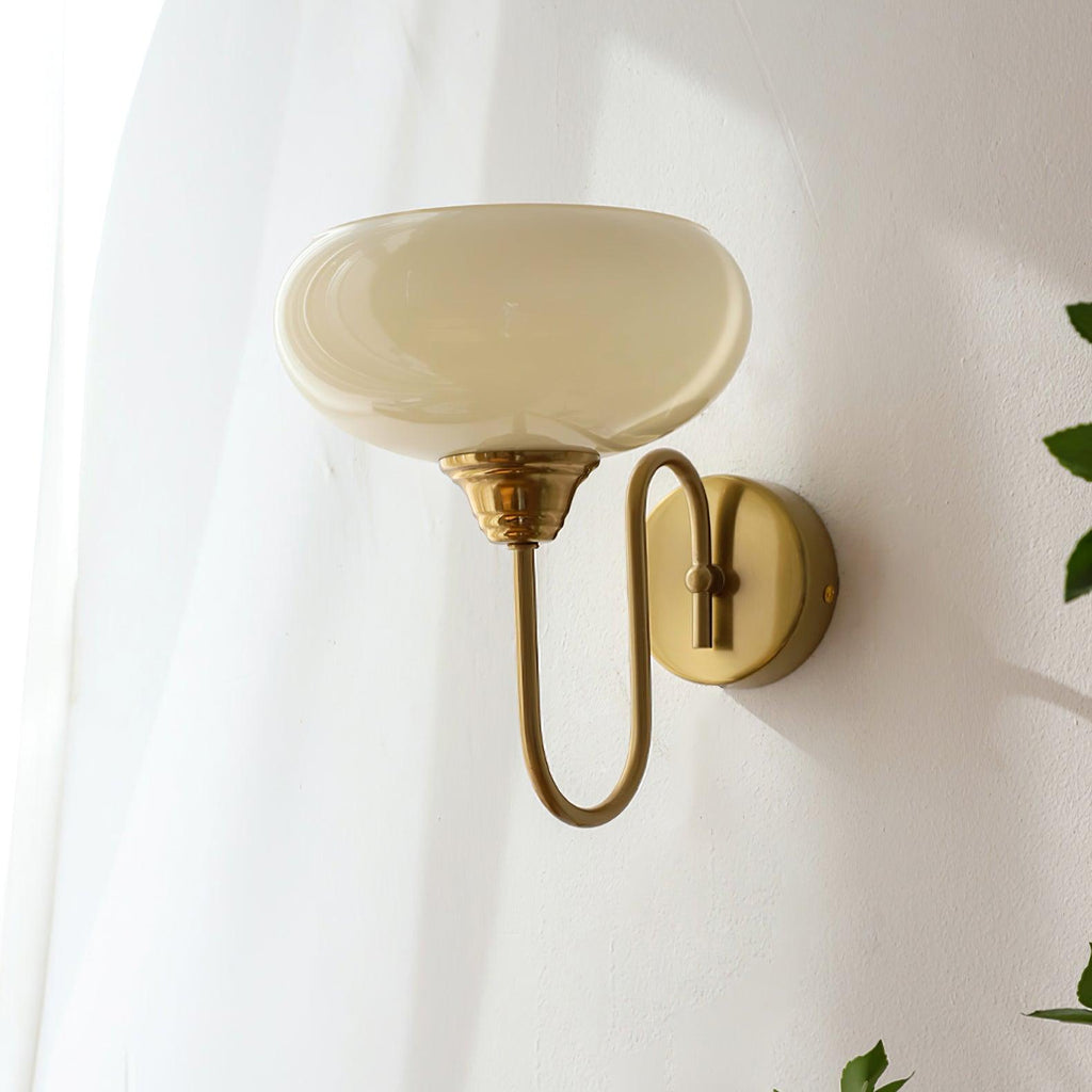 Clérachic glass wall lamp in copper with beige glass, hardwired U-arm seen beside a sheer curtain and leaves.